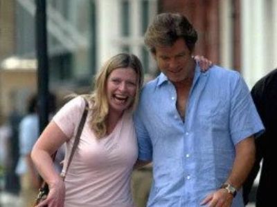 Charlotte Brosnan and Pierce Brosnan have their arms around each other as they are walking and laughing.